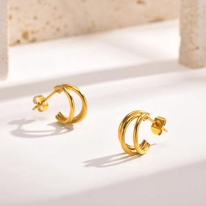 Détail des boucles d'oreilles double C plaquées or 18k sur un support en pierre blanche