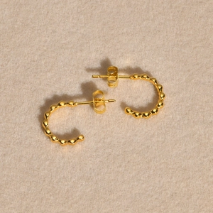 Boucles d'oreilles créoles C en acier inoxydable doré perlé sur fond en velours beige