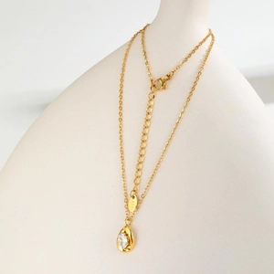Gold stainless steel teardrop necklace with oval white zircon on a minimalist white vase