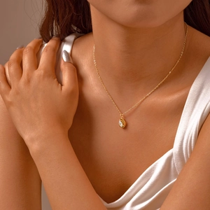 Detail of a woman wearing a gold necklace with a water drop pendant and clear zircon stone
