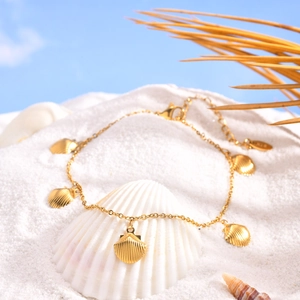 Detail of gold seashell anklet with fan-shaped pendants on white beach sand