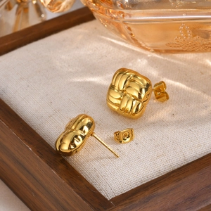 Détail des boucles d'oreilles dorées tissées géométriques dans un écrin en bois