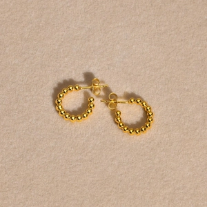 Boucles d'oreilles créoles dorées en C avec perles sur un fond neutre texturé
