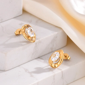 Detail of gold-plated stainless steel earrings with oval zircon on marble stand