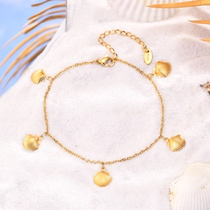Golden stainless steel shell anklet with five fan pendants on white sand beach background
