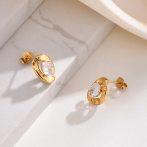 Detail of gold oval earrings with clear cubic zirconia on marble and silk surface