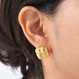 Gros plan de boucles d'oreilles carrées tressées dorées portées par une femme