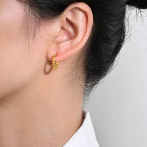 Boucles d'oreilles créoles dorées en perles d'acier inoxydable portées par un modèle