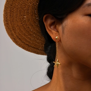Détail d'une boucle d'oreille étoile de mer dorée avec chaîne portée par un modèle