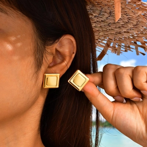 Close-up of geometric square gold earrings showing double-layered architectural metal design