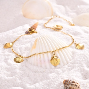 Detail of gold shell anklet with five textured pendants on white sand beach background