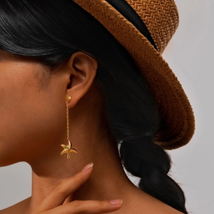 Détail des boucles d'oreilles pendantes étoile de mer dorées portées pour un style estival