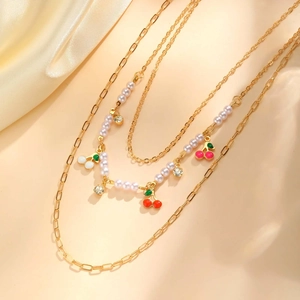 Detail of three-layer necklace with gold chains, faux pearls and cherry pendants
