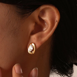Macro view of gold oval stud earring with white cubic zirconia on female ear lobe