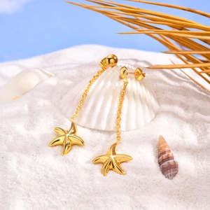 Vue détaillée de boucles d'oreilles étoile de mer dorées sur sable blanc avec coquillages