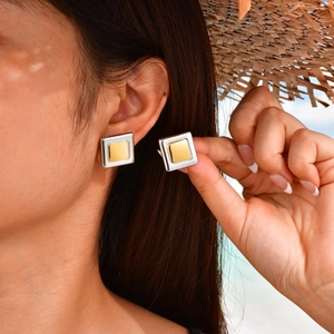 Close-up of minimalist square gold and silver metal stud earrings on a beach setting
