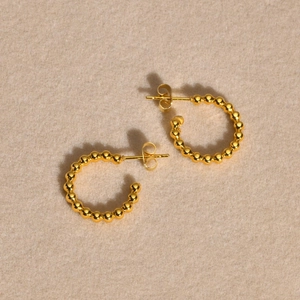 Vue détaillée des boucles d'oreilles C perlées dorées avec finition miroir sur velours