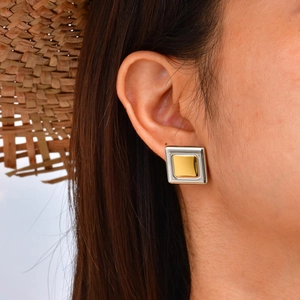 Close-up of a two-tone square stud earring in gold and silver finish on a model