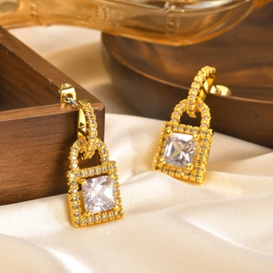 Macro detail of golden padlock earrings with square zircon and crystal pavé on silk