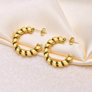 Detailed macro view of polished gold twisted C-shape hoop earrings on beige silk fabric