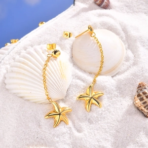 Détail de boucles d'oreilles étoile de mer dorées sur sable blanc et divers coquillages