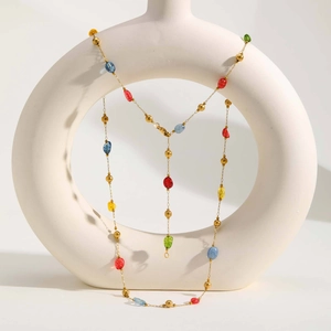 Dettaglio di collana a Y bohémien con pietre naturali colorate e perline dorate su un vaso
