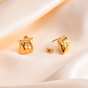 Close-up of golden square earrings with hammered texture on champagne silk fabric