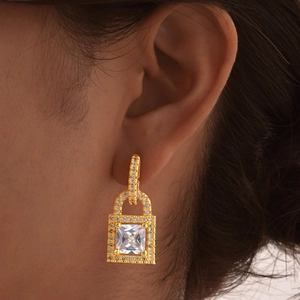 Close-up detail of golden padlock earrings with zircon stone worn by a model