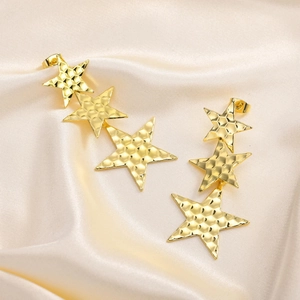 Long gold geometric star earrings with unique hammered texture on silky beige fabric