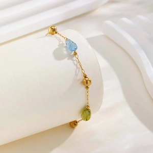 Dettaglio di bracciale in oro con pietre azzurre e verde oliva su supporto bianco
