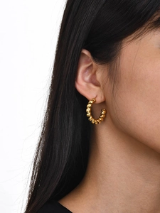 Close-up of gold twisted hoop earrings with a spiral texture worn by a model
