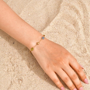 Dettaglio di bracciale a catena d'oro con gemme a goccia su una spiaggia soleggiata