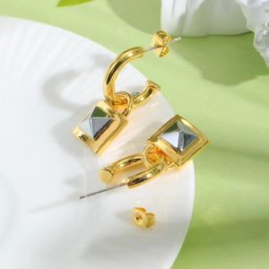 Nahaufnahme goldener geometrischer C-Ohrringe mit Pyramiden-Nieten auf weißem Teller