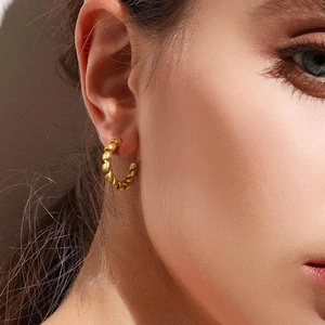 Close-up of gold-plated twisted rope hoop earrings worn by a model on neutral background