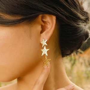 Fashionable gold triple star drop earrings with hammered finish for women worn by a model