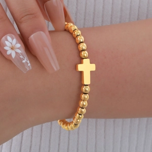 Bracelet à billes dorées pour femme avec pendentif croix minimaliste porté au poignet