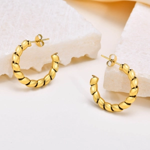 Close-up of golden C-shaped twisted earrings with a polished metallic finish on stone