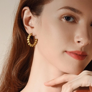 Detailed view of a model wearing golden twisted rope hoop earrings in a minimalist style