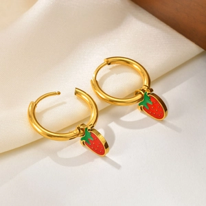 Détail de boucles d'oreilles fraise en émail rouge sur un fond de tissu en soie blanche