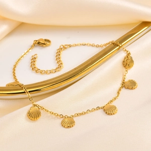 Gold shell anklet featuring five scallop pendants on a delicate chain over silk background