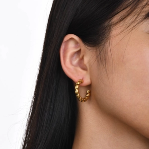 Fashionable gold-tone stainless steel twisted hoop earrings on a female model
