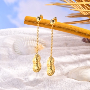 Detailed close-up of 18K gold peanut tassel earrings hanging on a beach branch decor