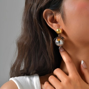 Minimalist gold and silver spherical drop earrings with amber floral accents on a model