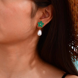 Detail of elegant gold drop earrings with green floral motif and large teardrop pearls