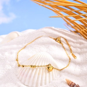 Bracelet de cheville doré avec cœur sur sable blanc avec coquillages et décorations
