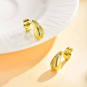 Detail view of gold drop earrings with vertical zircon inlay on a white ceramic plate