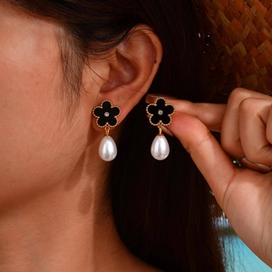 Elegant gold flower earrings with black petals and teardrop pearls worn by a model