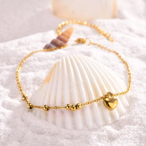 Bracelet de cheville doré avec cœur et perles présenté sur des coquillages de mer