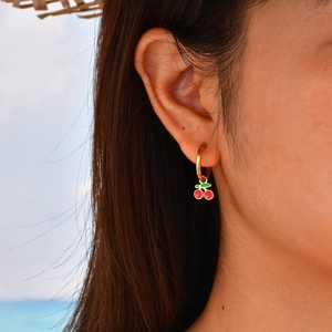 Gros plan de boucles d'oreilles cerises rouges portées par un mannequin en extérieur