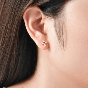 Détail d'une boucle d'oreille croix dorée avec zircons étincelants et une pierre rouge
